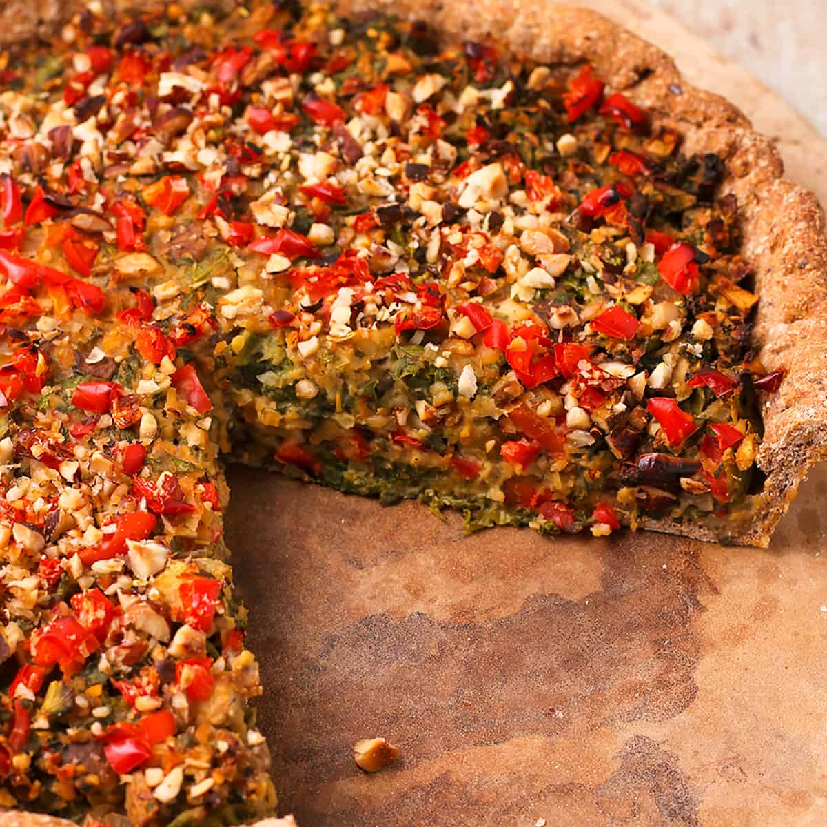A baked vegan quiche with mushrooms and kale is cut and placed on a stone.