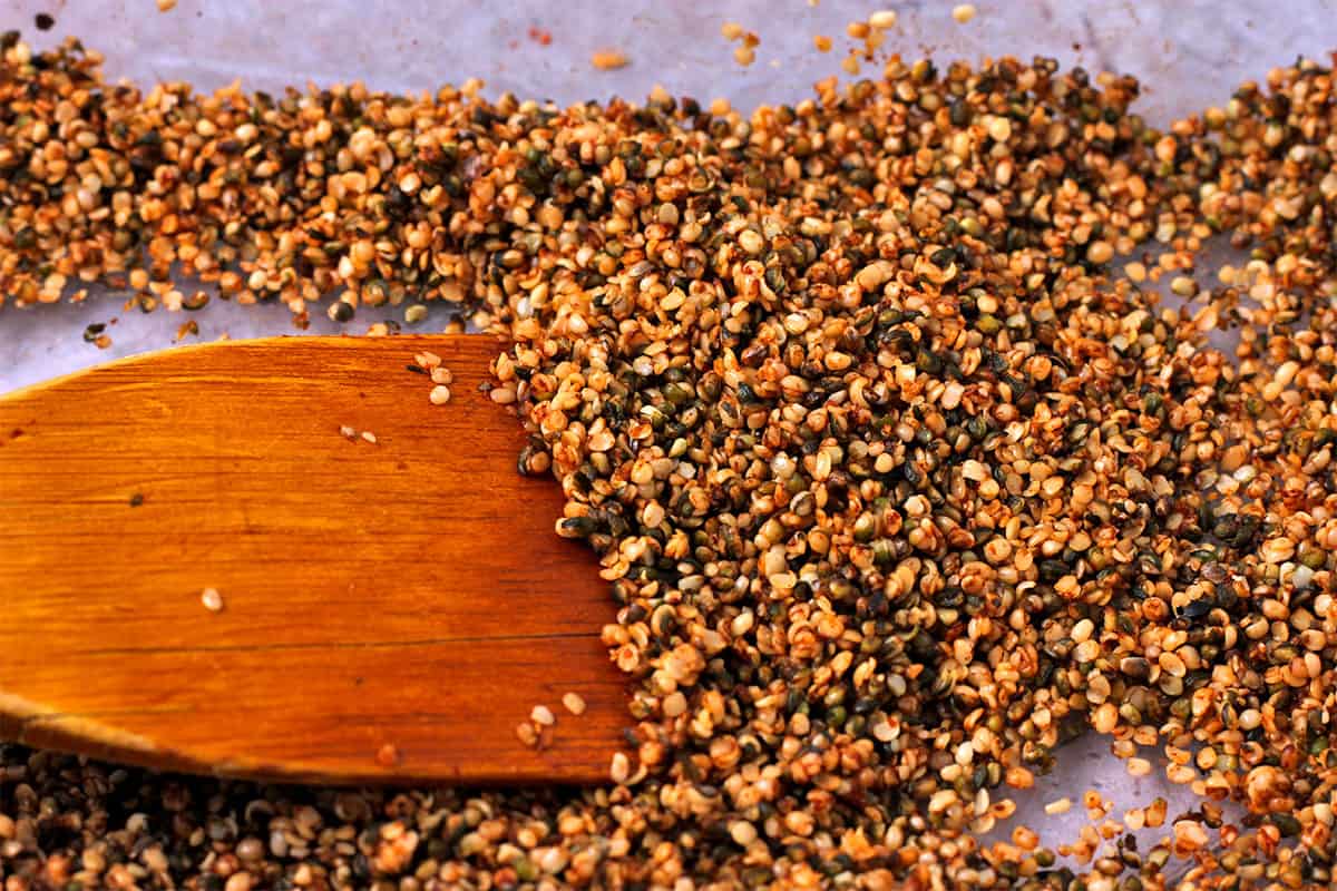 Baked hemp seed bacon bits in a glass baking dish are stirred with a wooden spatula.
