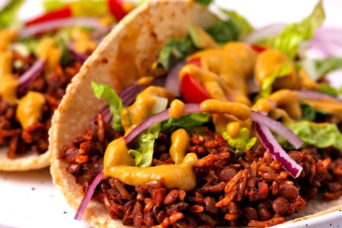 A taco with vegan taco meat, avocado dressing red onions, lettuce, and tomatoes.