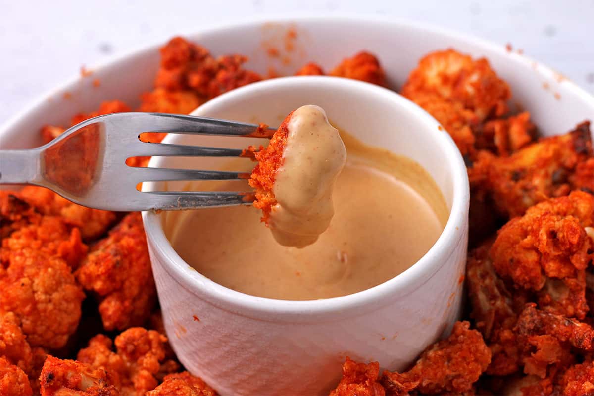 A spicy cauliflower wing is dipped in peanut sauce.