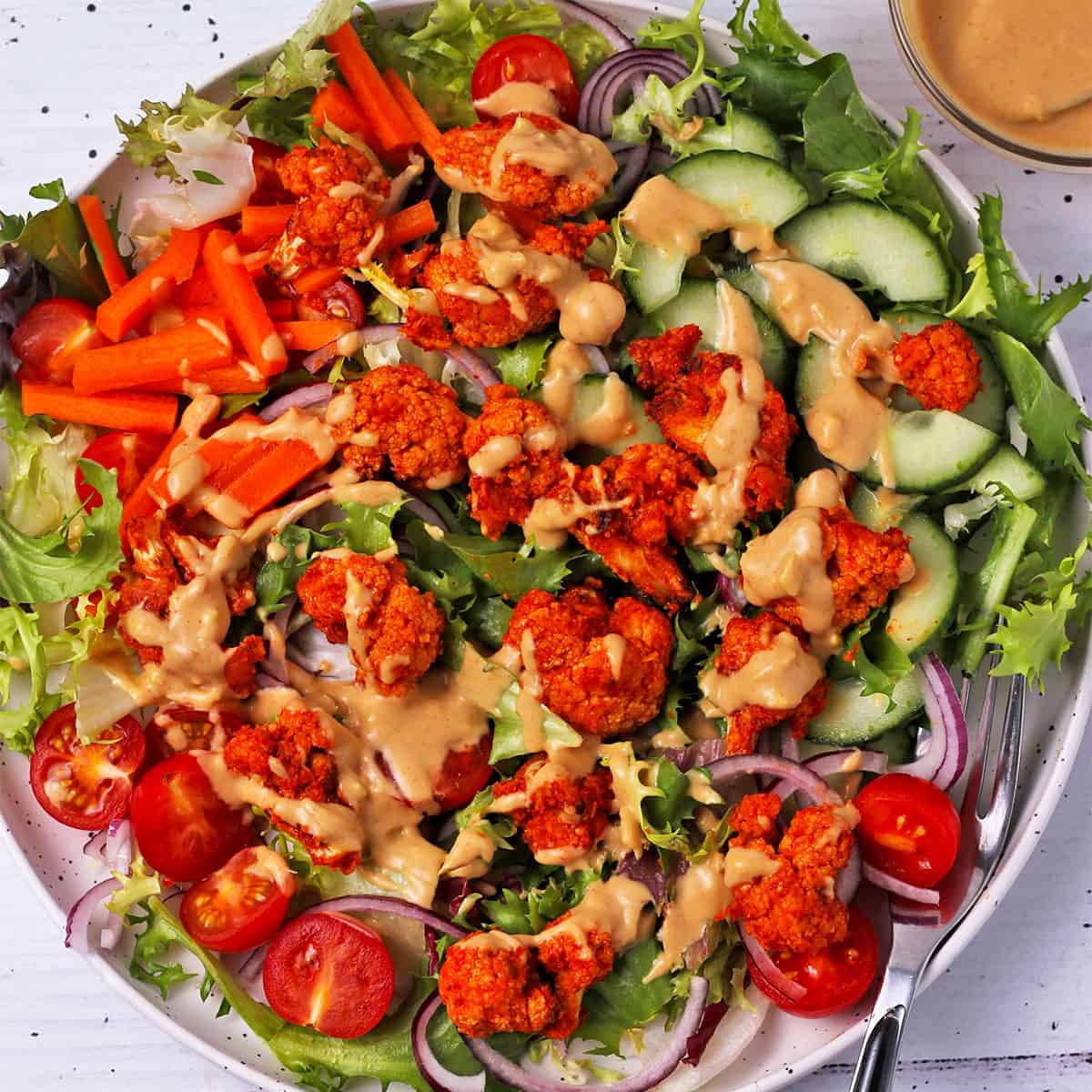 Spicy cauliflower wings over a green vegetable salad with peanut dressing.