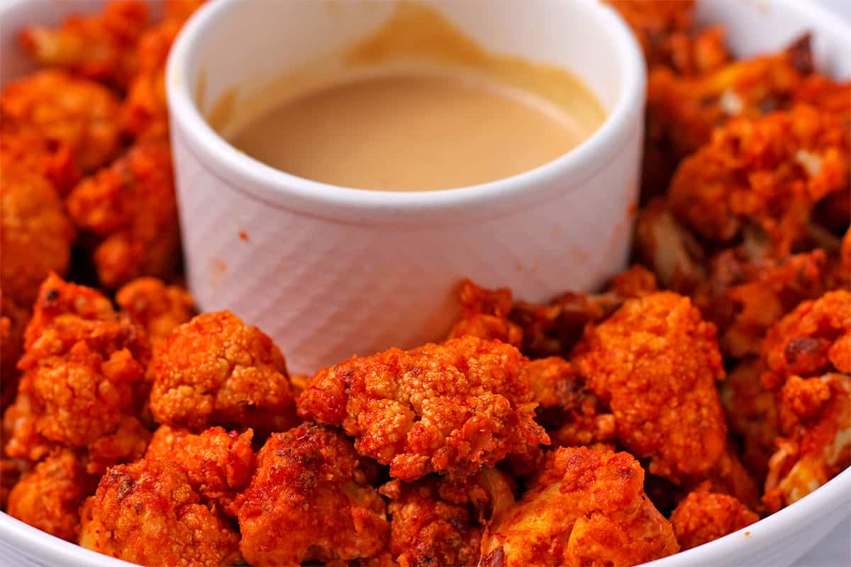 Cauliflower bites with spicy sauce and peanut dipping sauce in a white bowl.