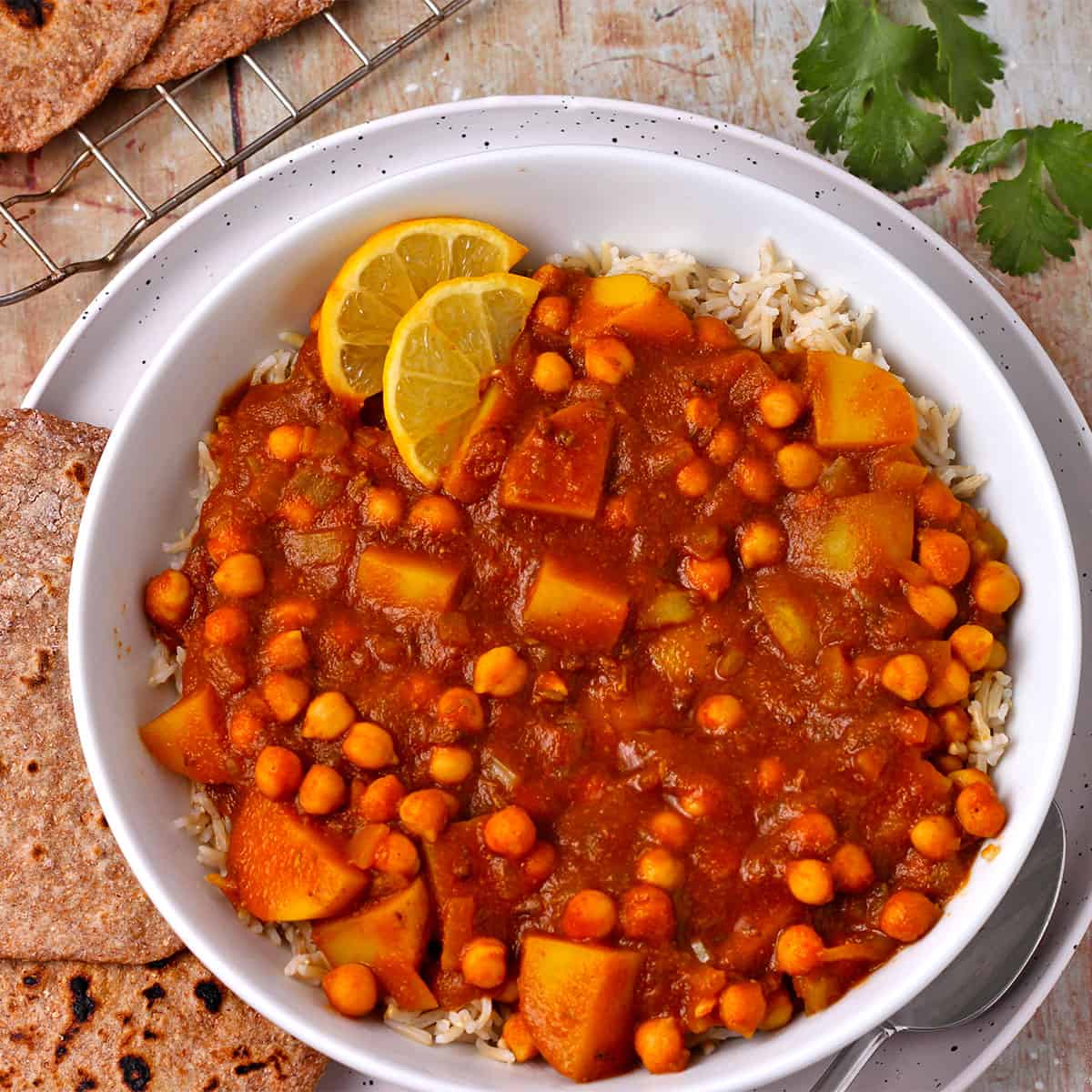 Overhead view of potato and chickpea curry in white bowl with brown rice.